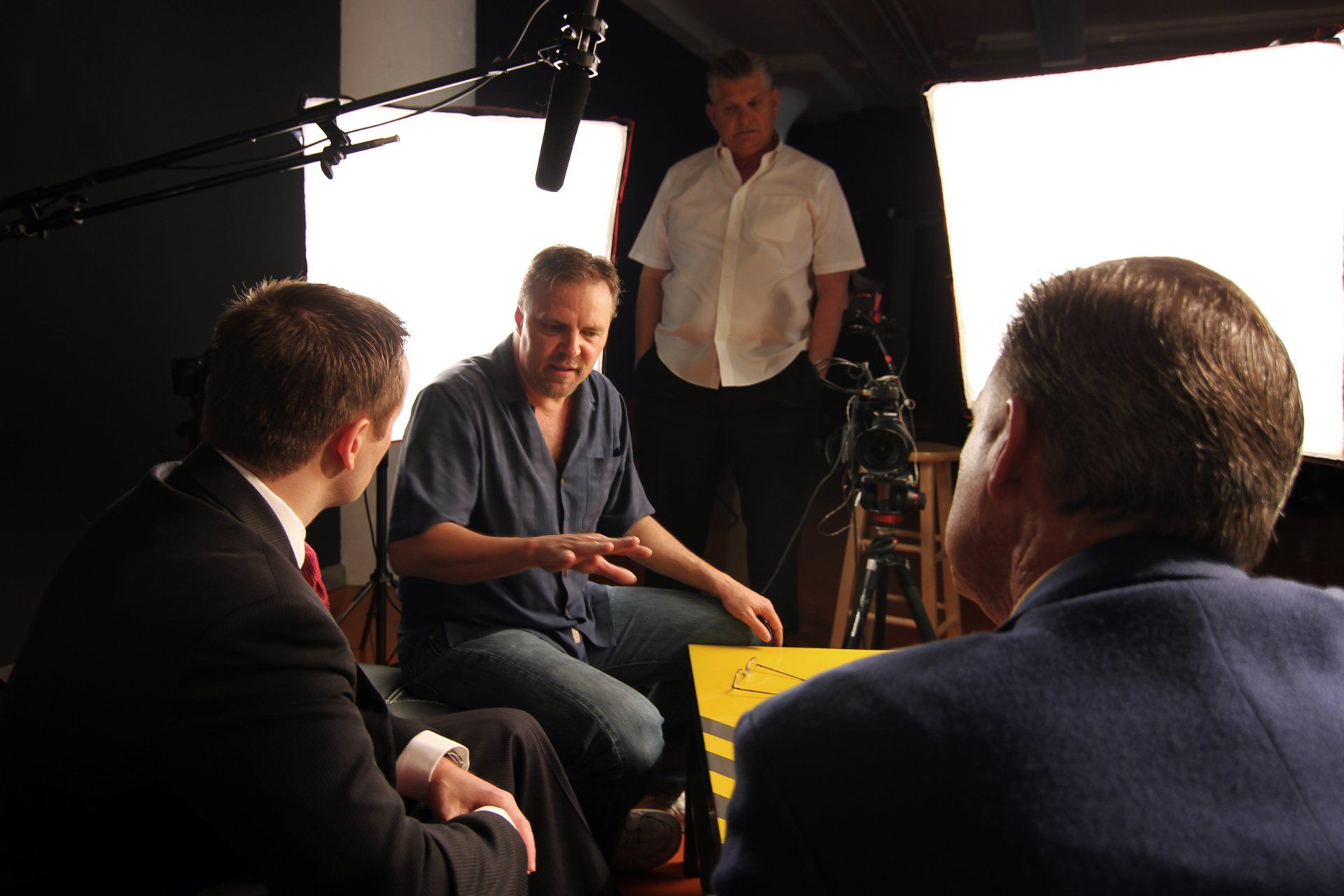 A man sitting on a film set directing two men before they film.