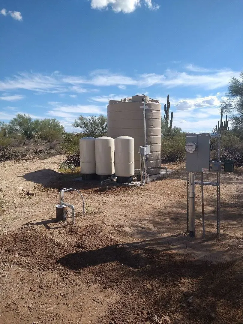Water tanks and equipment on a dirt lot under a blue sky, surrounded by desert vegetation.
