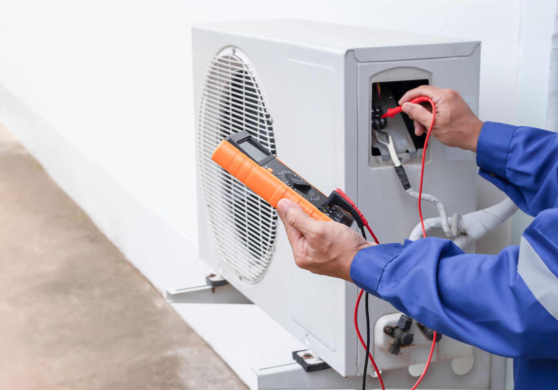 HVAC technician in blue coveralls using a multimeter to test an outdoor air conditioning unit. HVAC technician in blue coveralls using a multimeter to test an outdoor air conditioning unit.