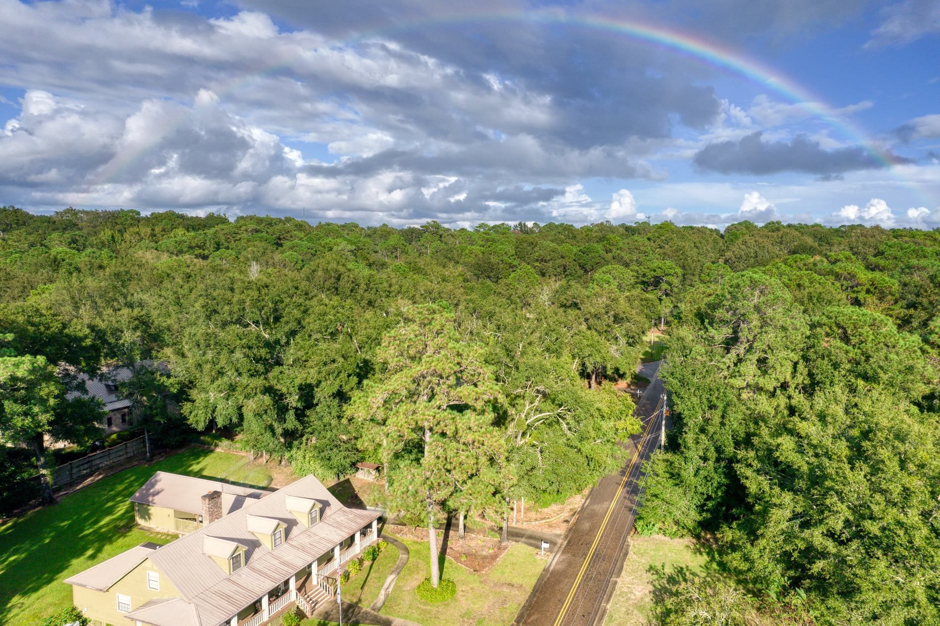 An aerial view of a house in the middle of a forest with a rainbow in the sky