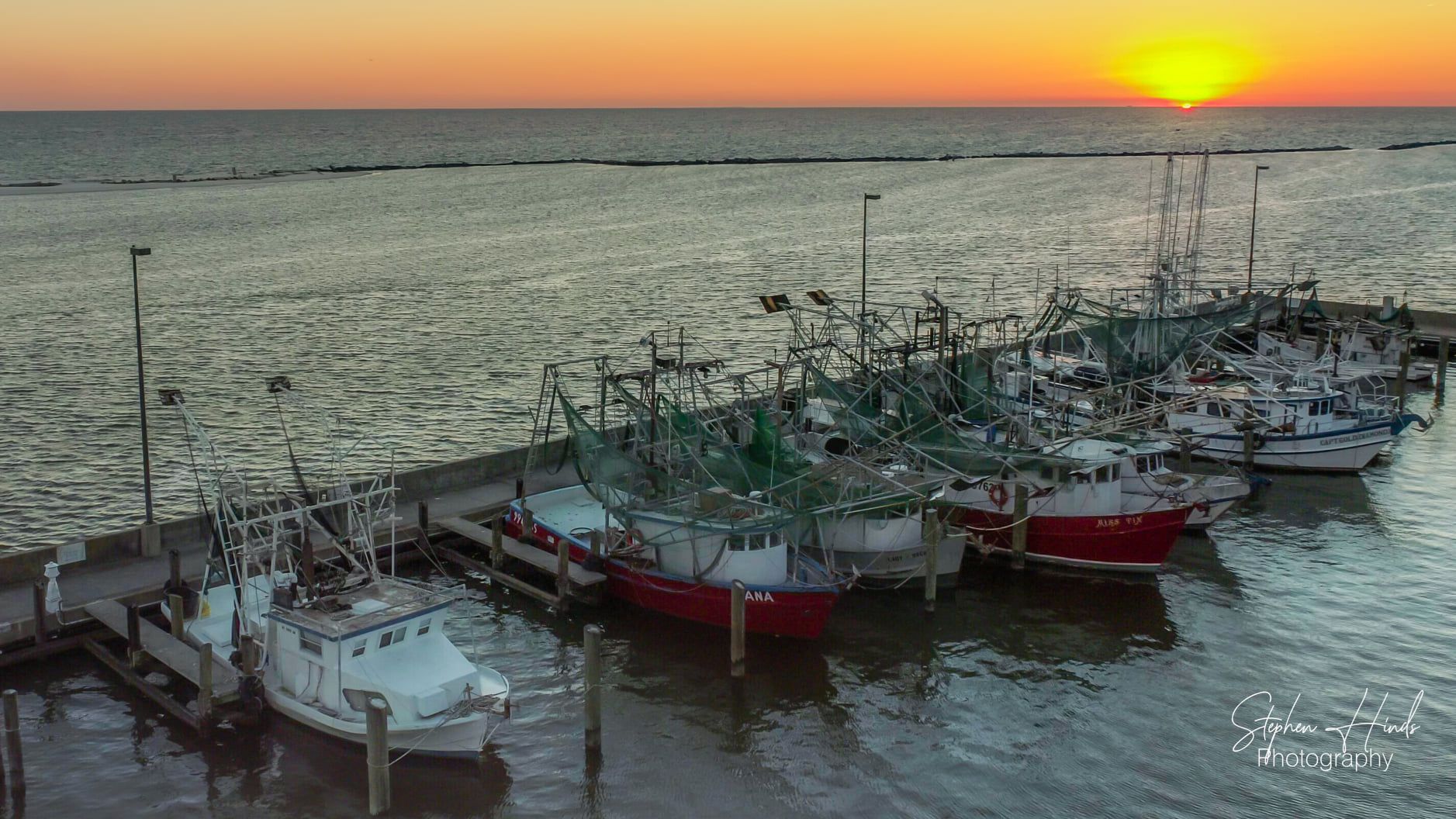 A group of boats are docked at a dock with the sun setting in the background