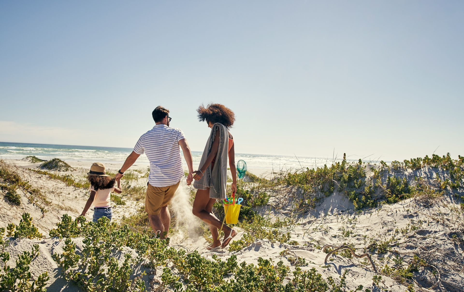 A family walks down a sandy hill towards the ocean