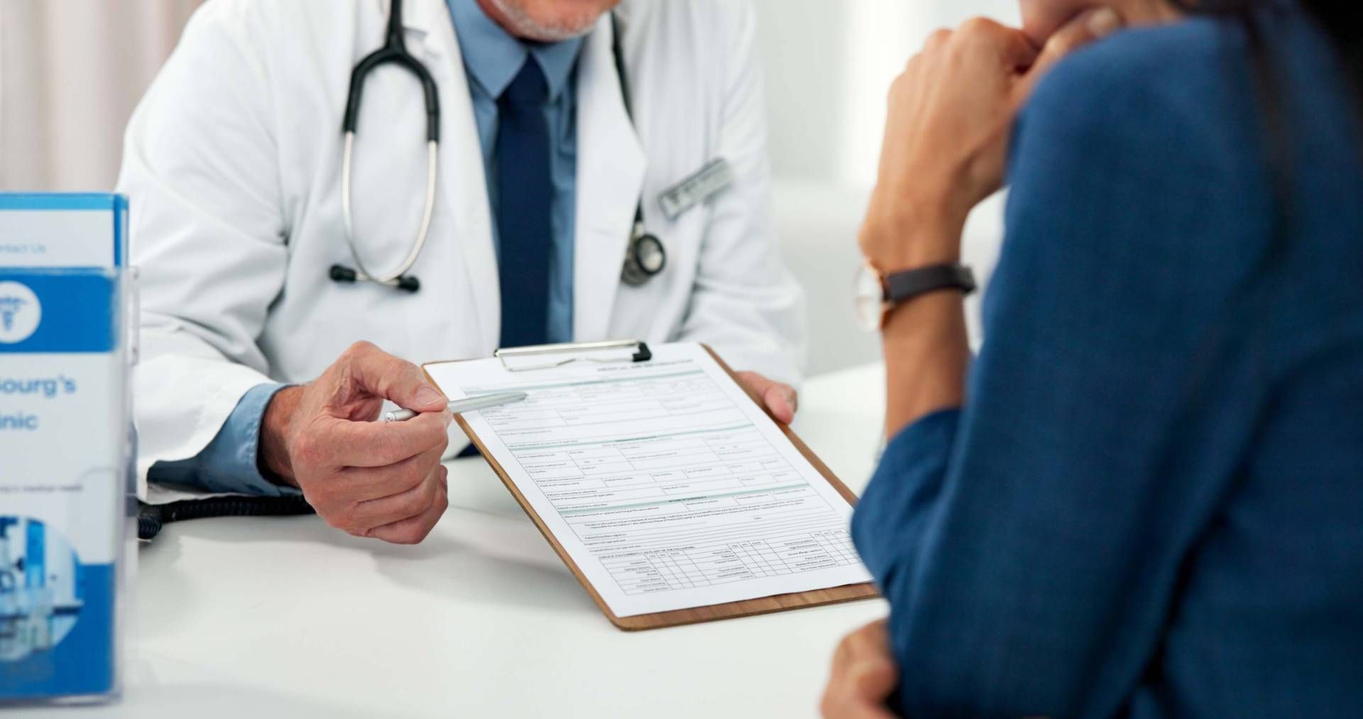 Doctor in white coat reviewing paperwork with a patient across a desk in a medical office.