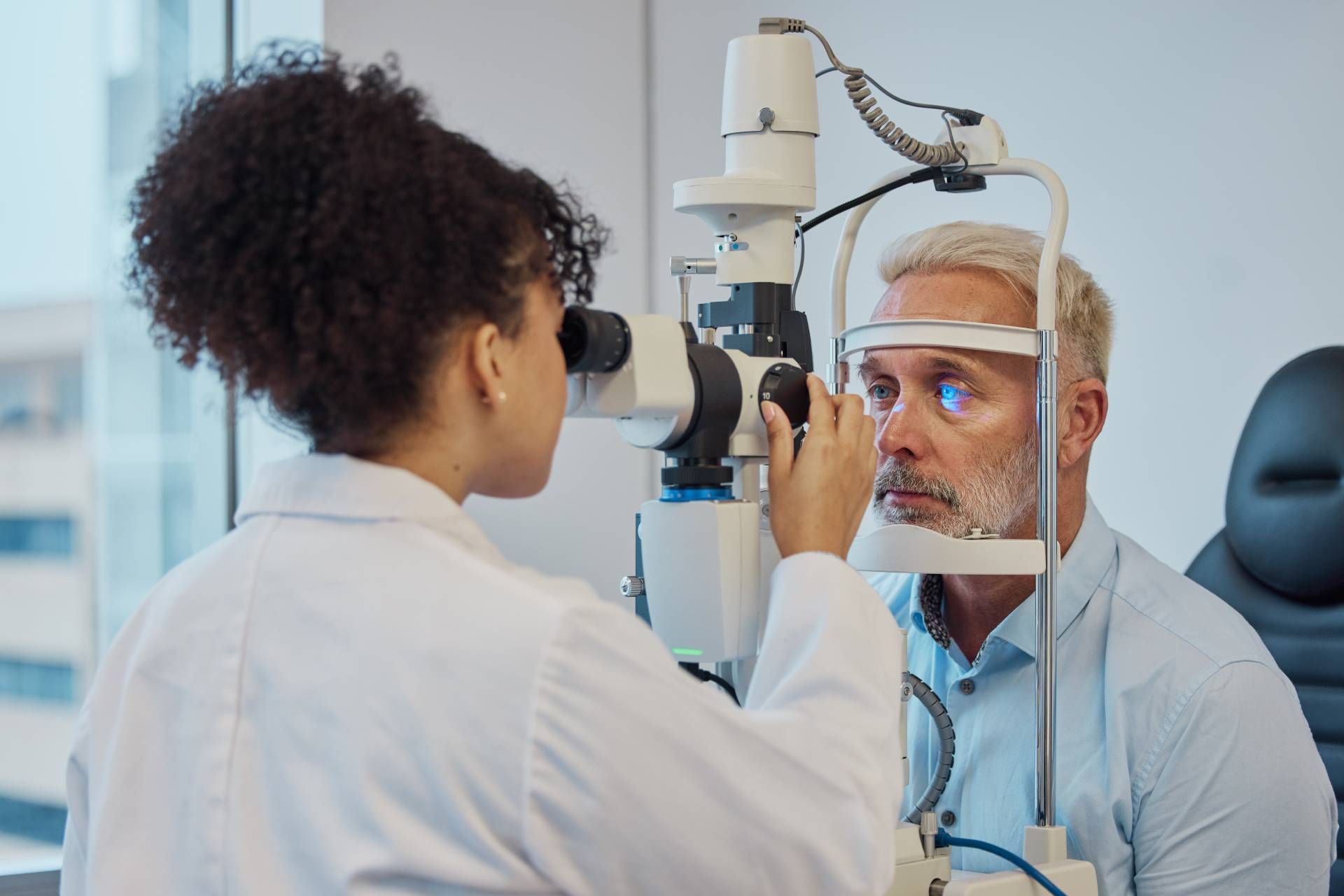 Eye exam with ophthalmologist examining a patient through a slit lamp microscope