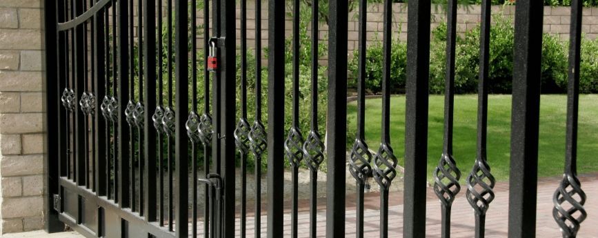 A close up of a wrought iron gate with a brick wall in the background.