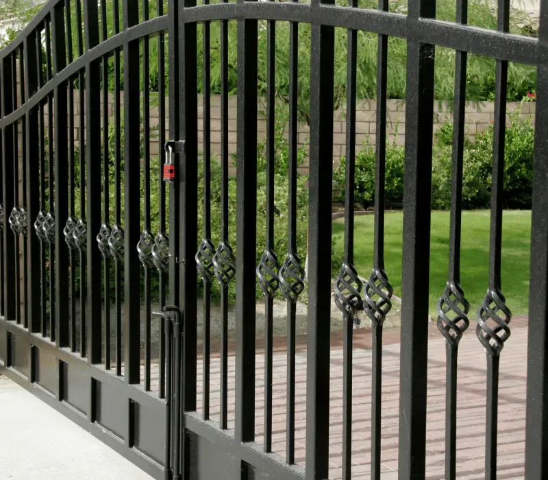 A black wrought iron gate is open to a driveway.