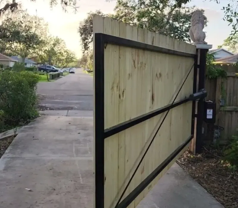 A wooden gate is open to a driveway with a statue of a lion in the background