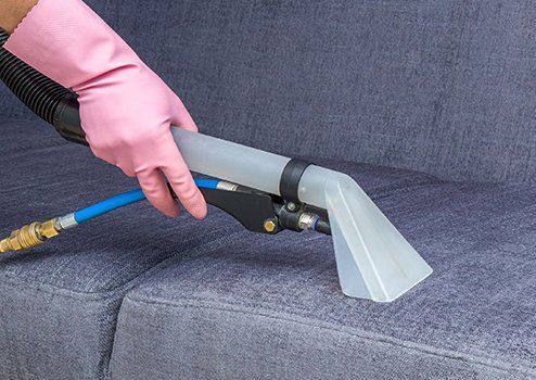 A Woman is Cleaning a Couch With a Vacuum Cleaner