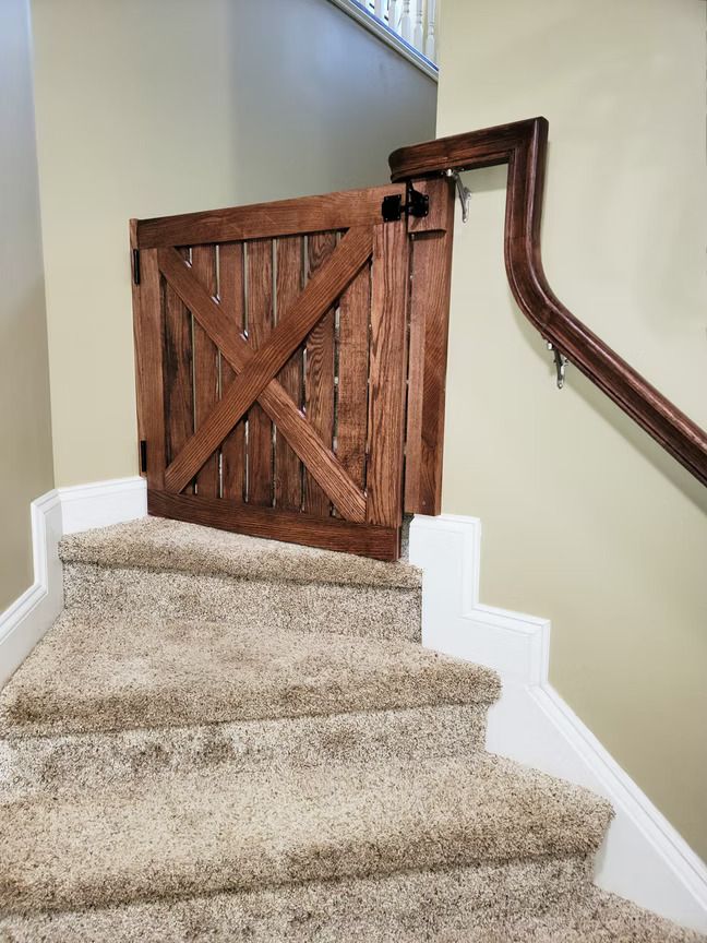 Wooden baby gate at the top of a carpeted staircase with a handrail on the right