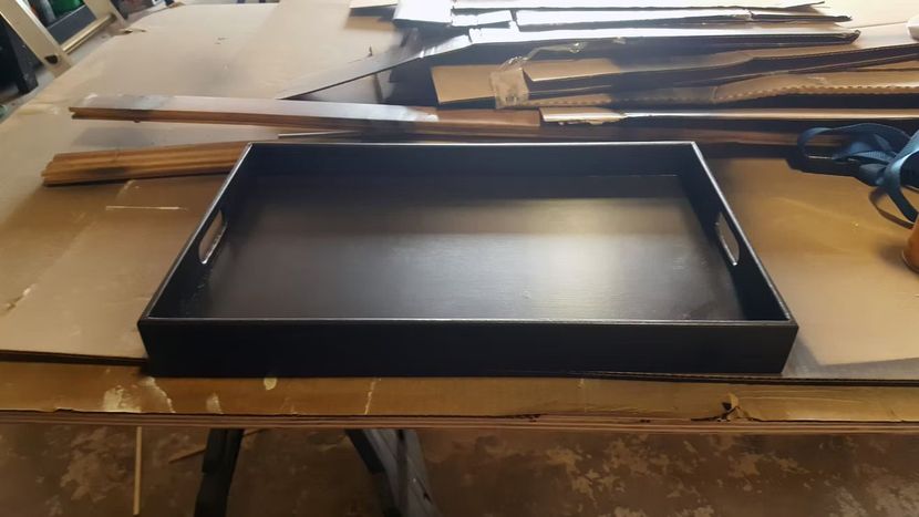 Black tray centered on a cluttered workbench with cardboard and tools around it.