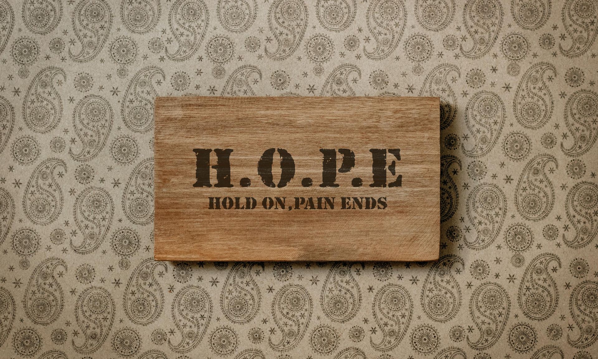 Wooden plaque reading “H.O.P.E.” on patterned wallpaper background.