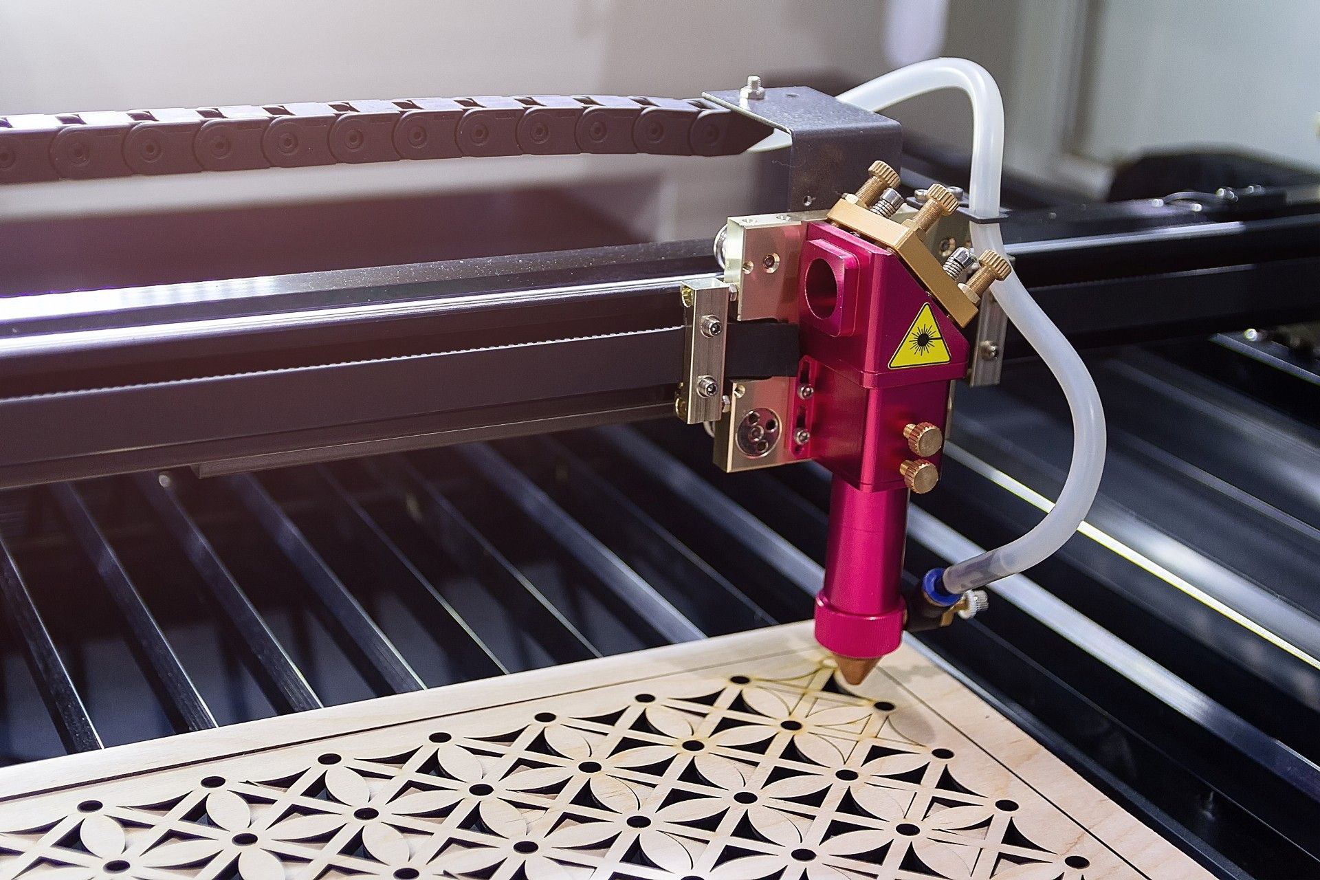 Laser cutter engraving a patterned design on a sheet with a red cutting head and honeycomb bed
