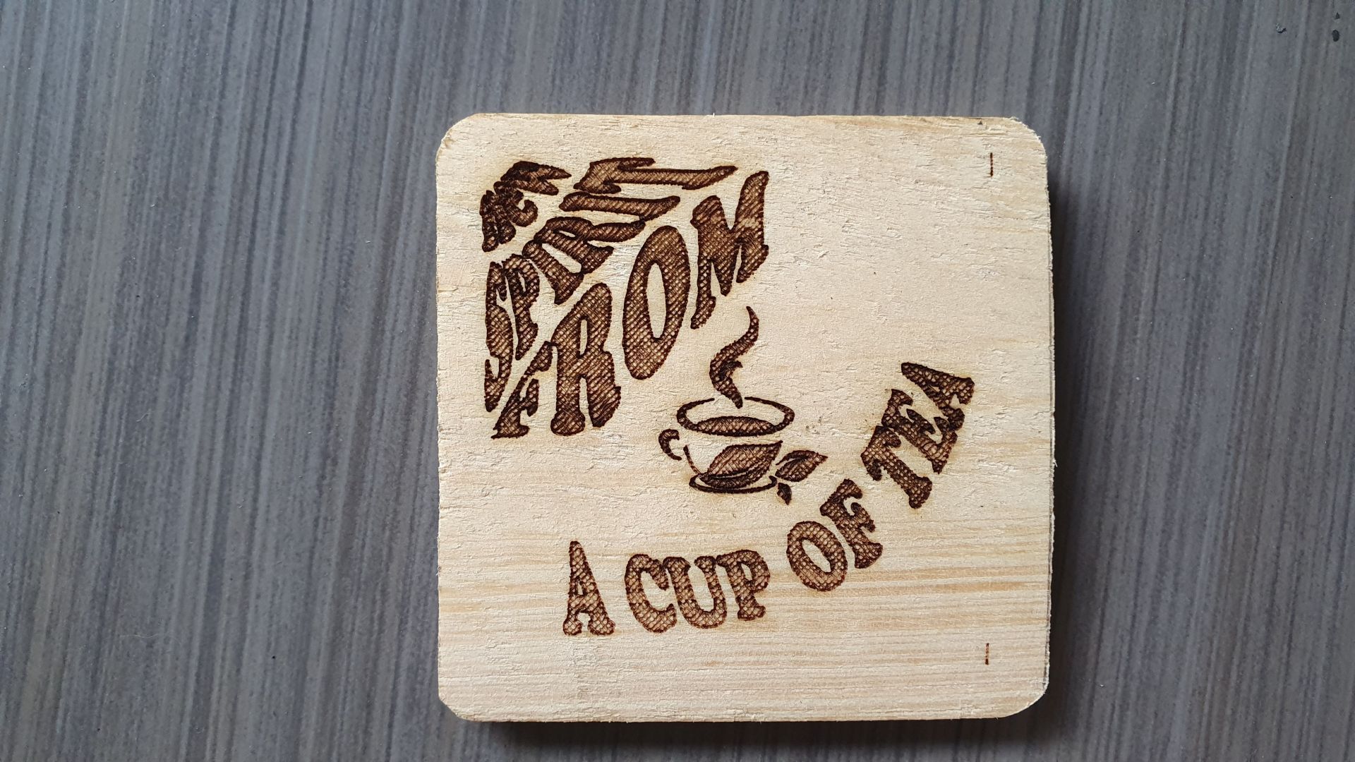 Wooden coaster with “I AM A CUP OF TEA” text and a steaming tea cup icon.