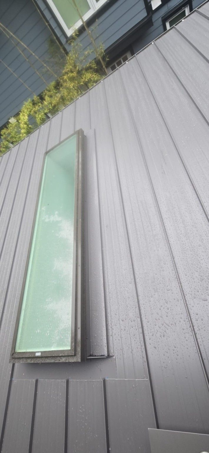 Raised seam metal panels beside a skylight and blue siding