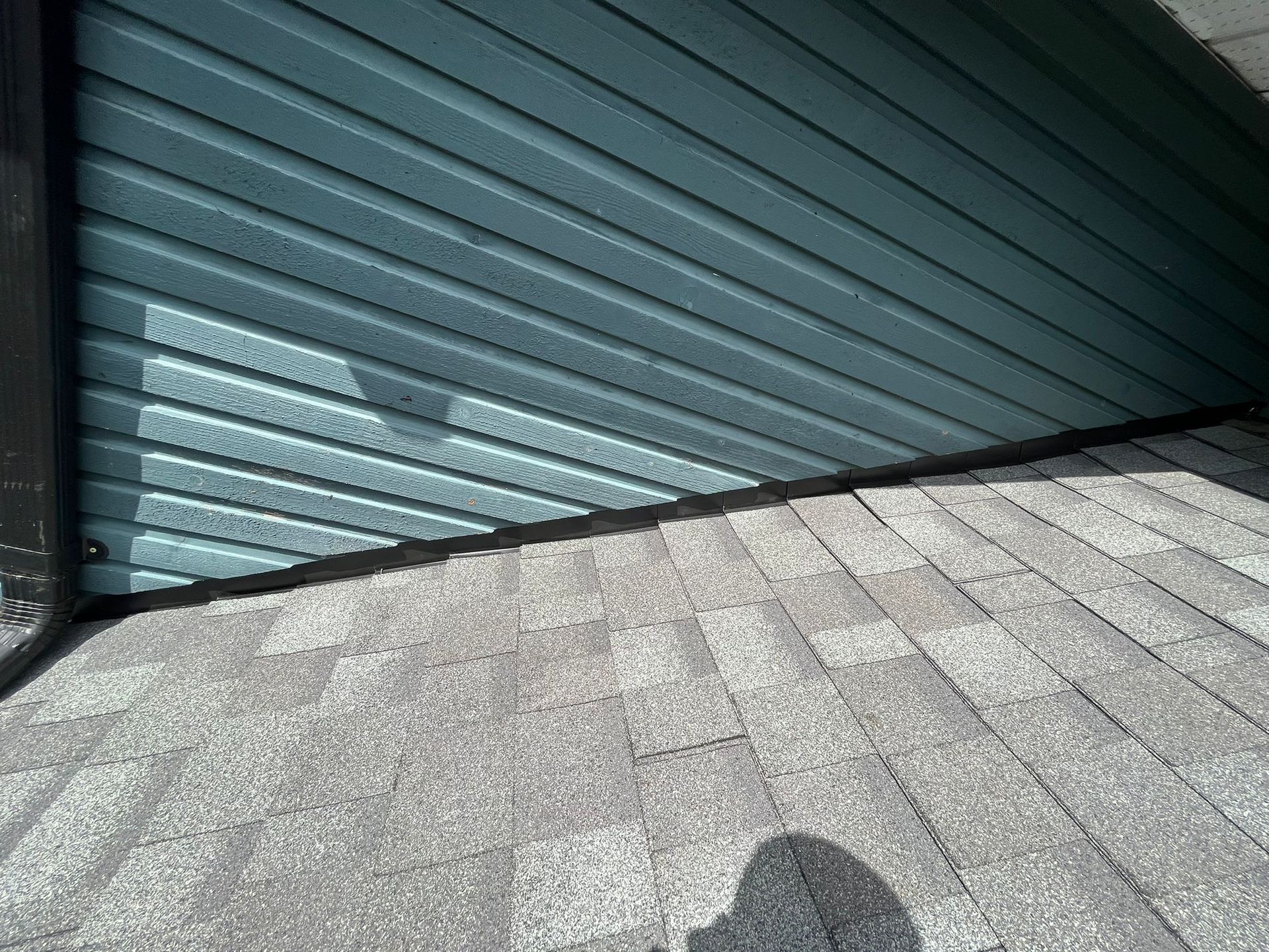 A close-up view of blue horizontal siding meeting a gray shingled roof at an angle, with a dark flashing strip.