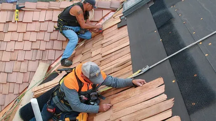Two roofers in safety gear installing terracotta tiles on a steep roof.