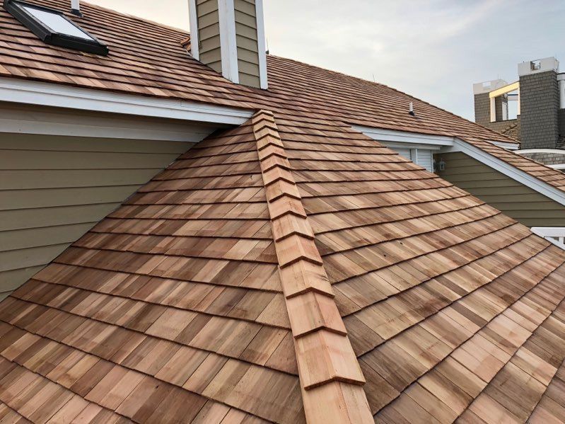 Wooden shingle roof with a central ridge, skylight, and chimneys on a building.