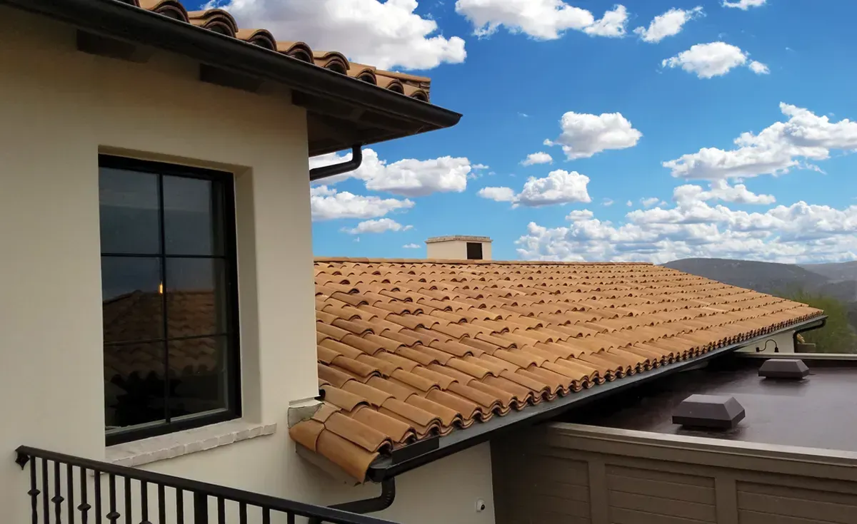 A roof with a vent on it and a building in the background.