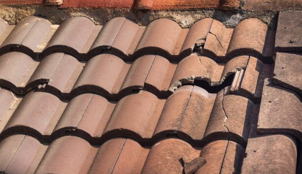 Several terracotta-colored roof tiles are cracked and broken, exposing the underlying roof structure.
