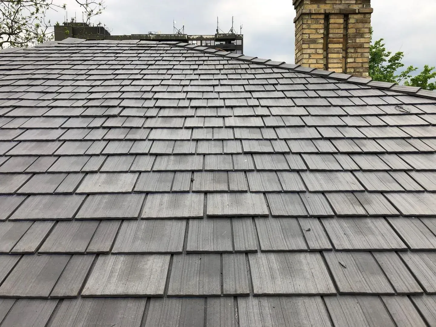 Gray wooden shingle roof with a brick chimney in the background.