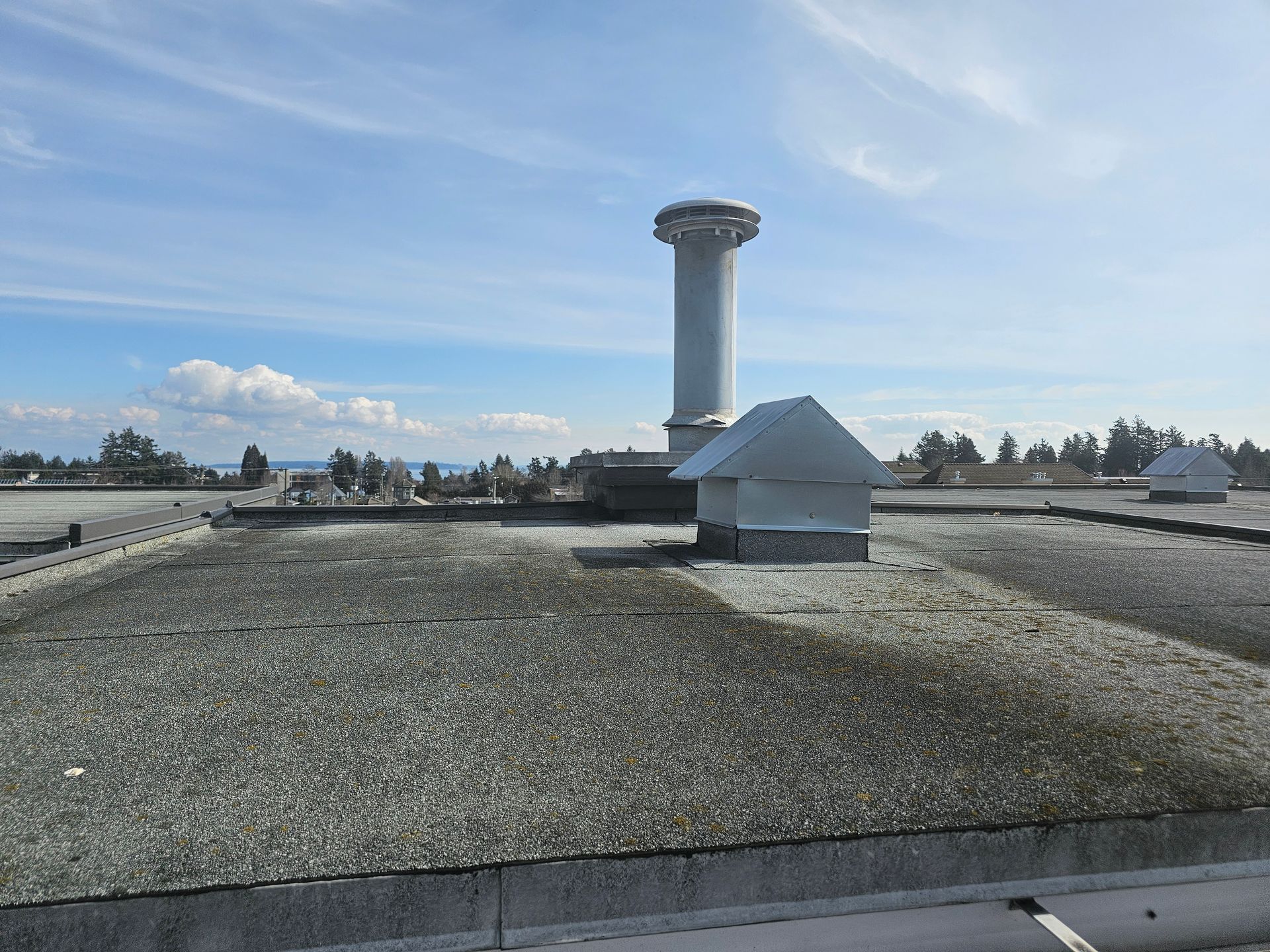 Flat roof with a tall white chimney and vents against a blue sky.