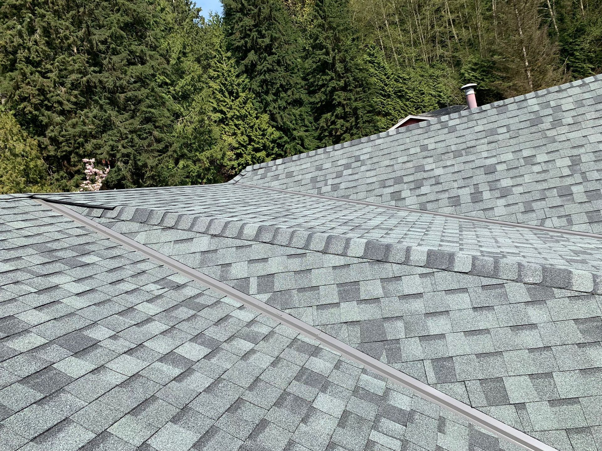 A close up of a roof with a lot of shingles and trees in the background.