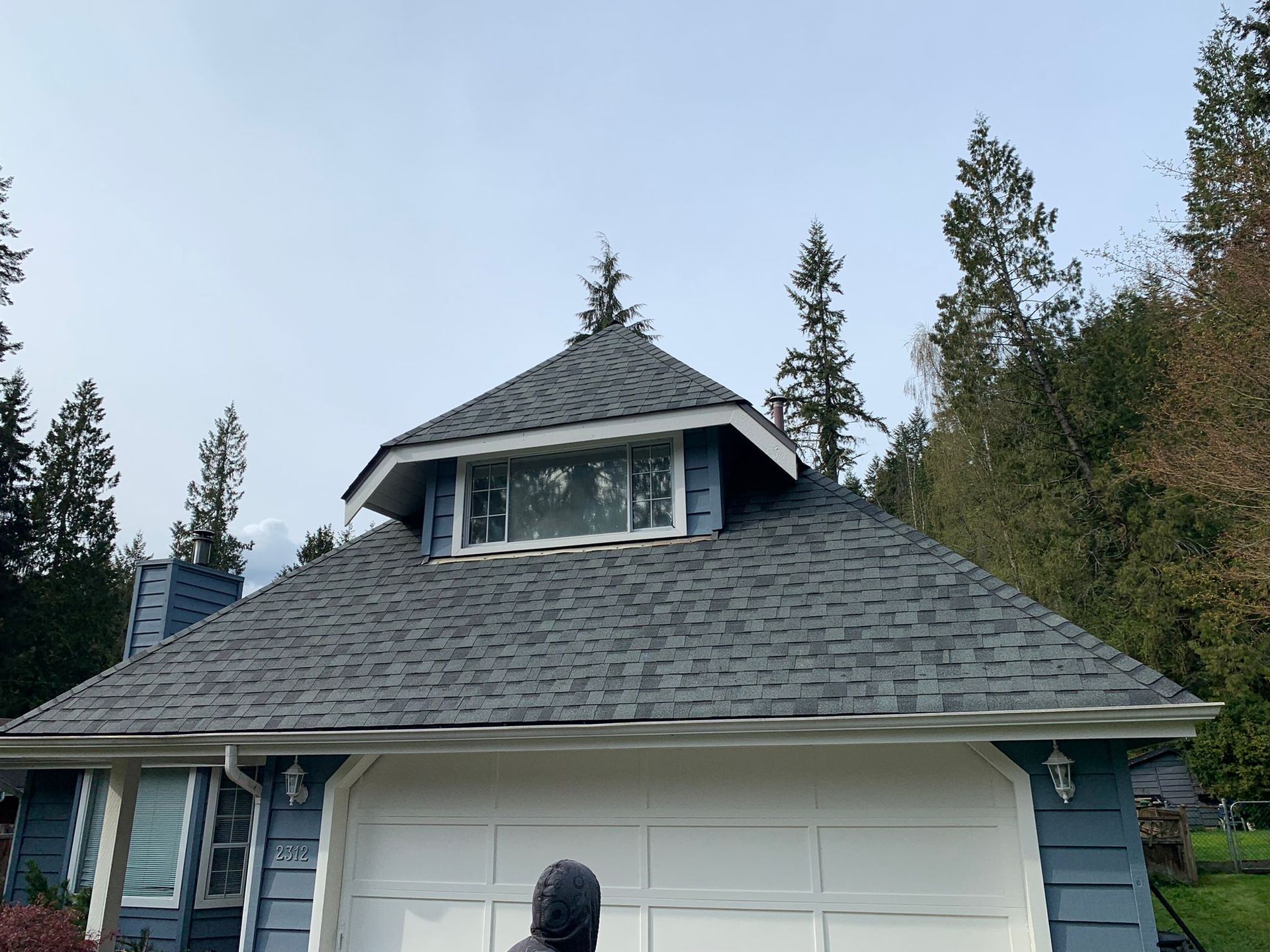 A man is standing in front of a house with a roof that is covered in shingles.