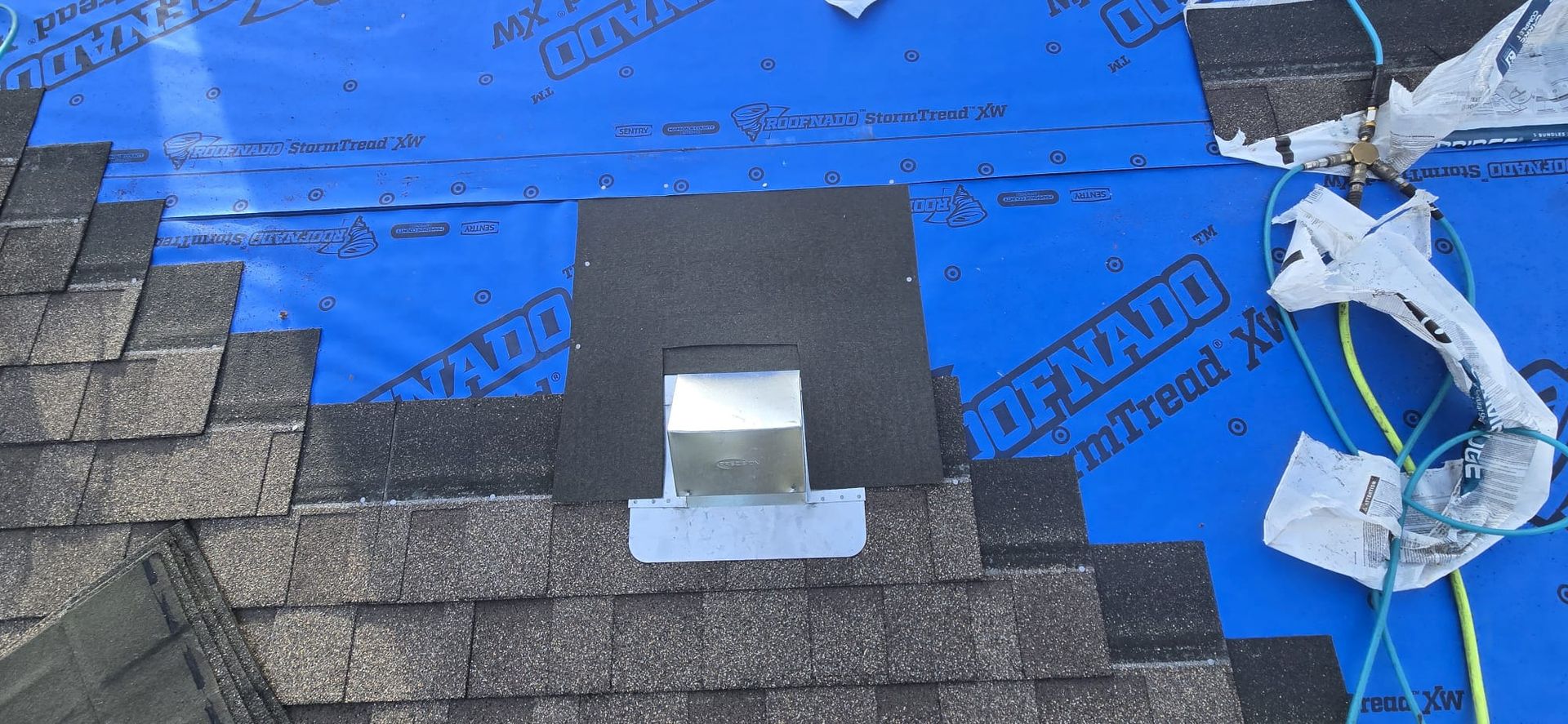 Shingles and blue underlayment around a roof vent during installation