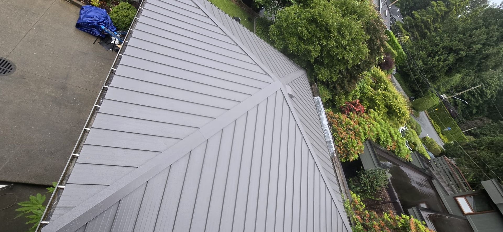 Grey metal roof with raised seams, a hip and eaves above a landscaped garden
