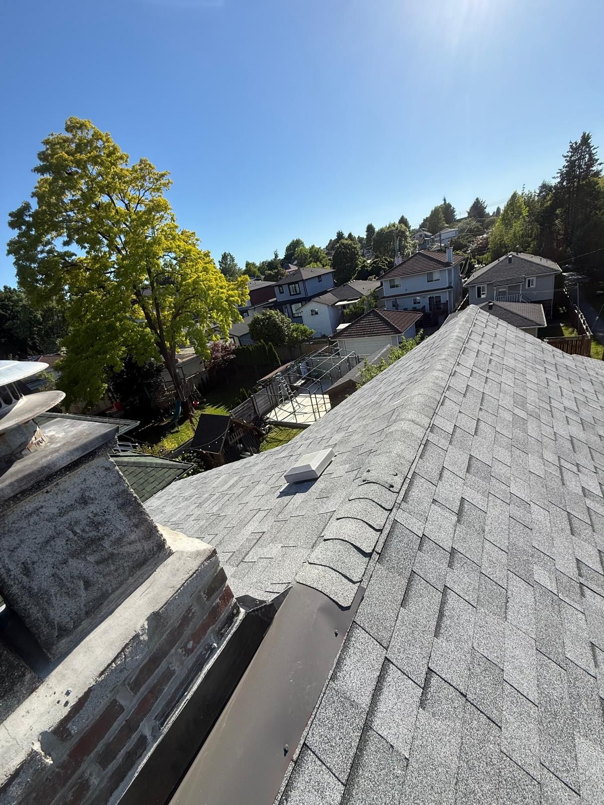 Grey shingle roof with ridge caps, a roof vent and chimney flashing