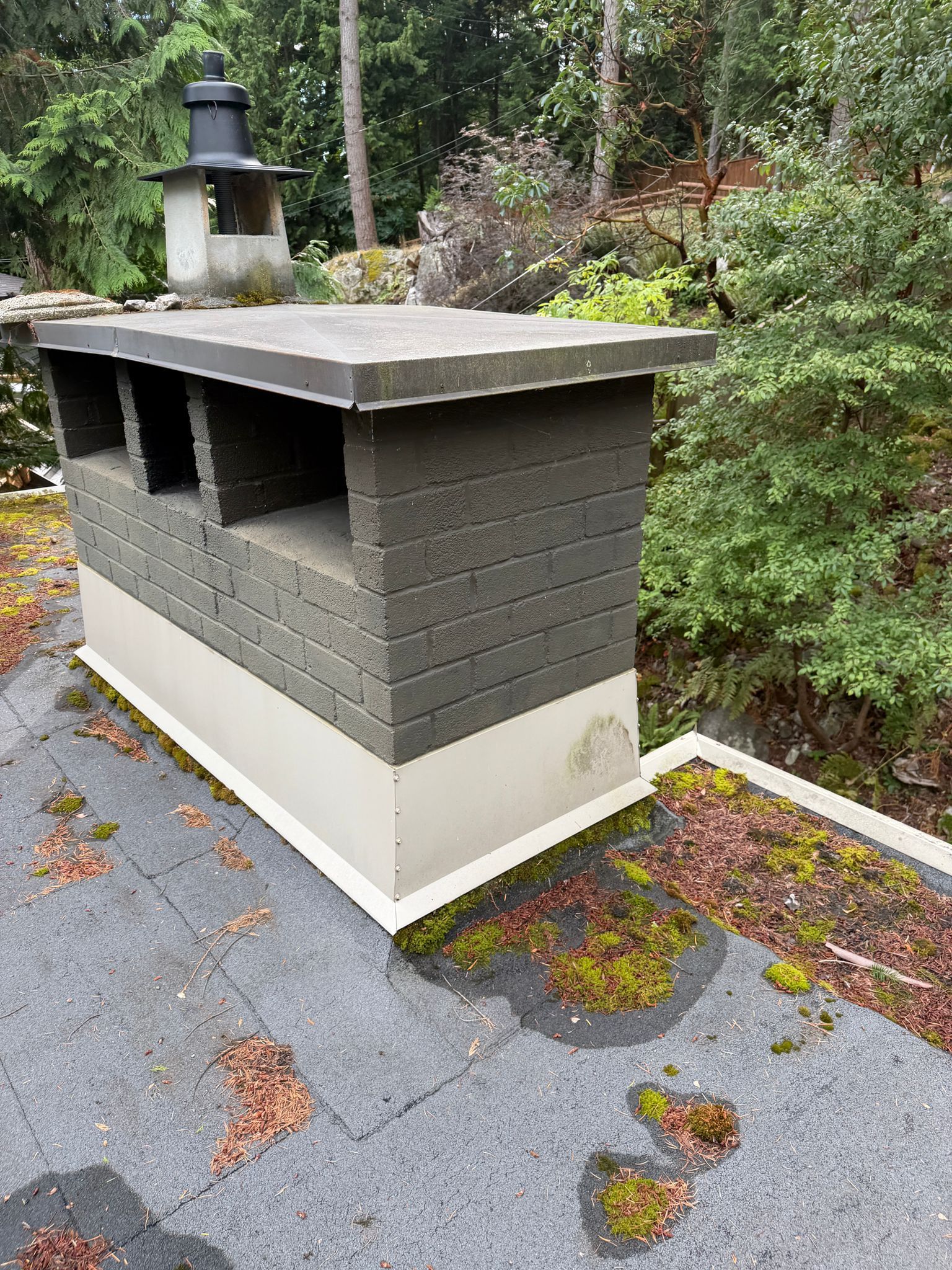 Masonry chimney with a metal cap and base flashing on an older roof