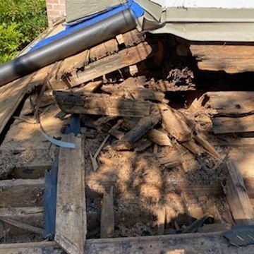 A section of a damaged, decaying roof structure with exposed wooden beams and rotted decking panels.