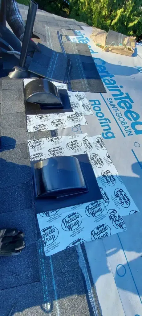 A roofing worker installs black roof vents onto a surface covered with CertainTeed brand underlayment.