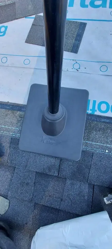 A roof vent pipe flashing installed on a shingled roof with underlayment visible above it.