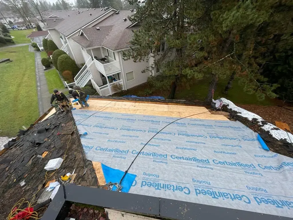 Construction workers installing roofing underlayment on a steep house roof.