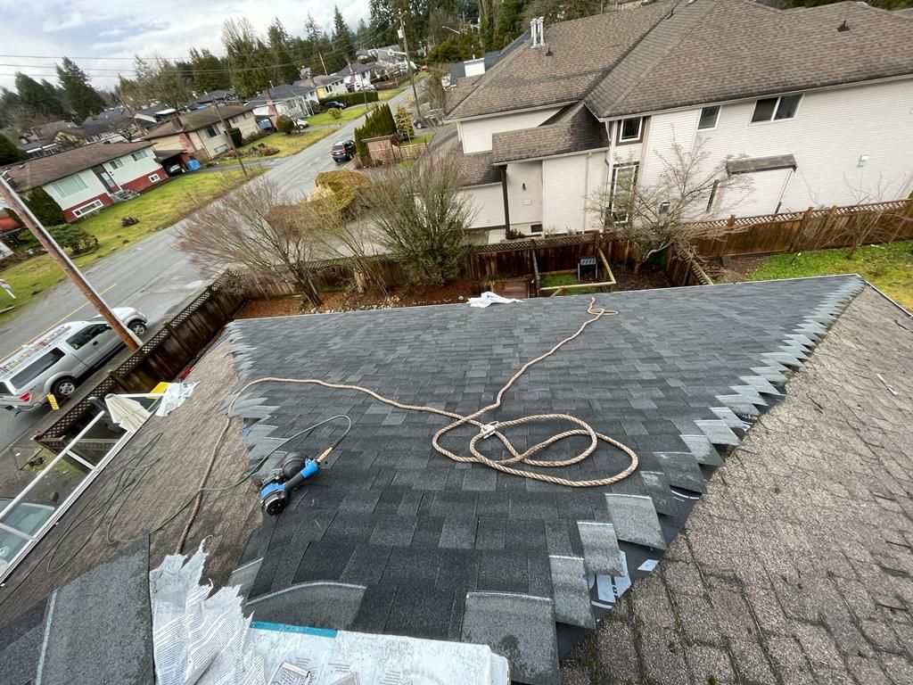 A high-angle view of a residential roof under repair, featuring new dark shingles, a coiled rope, and a power tool.