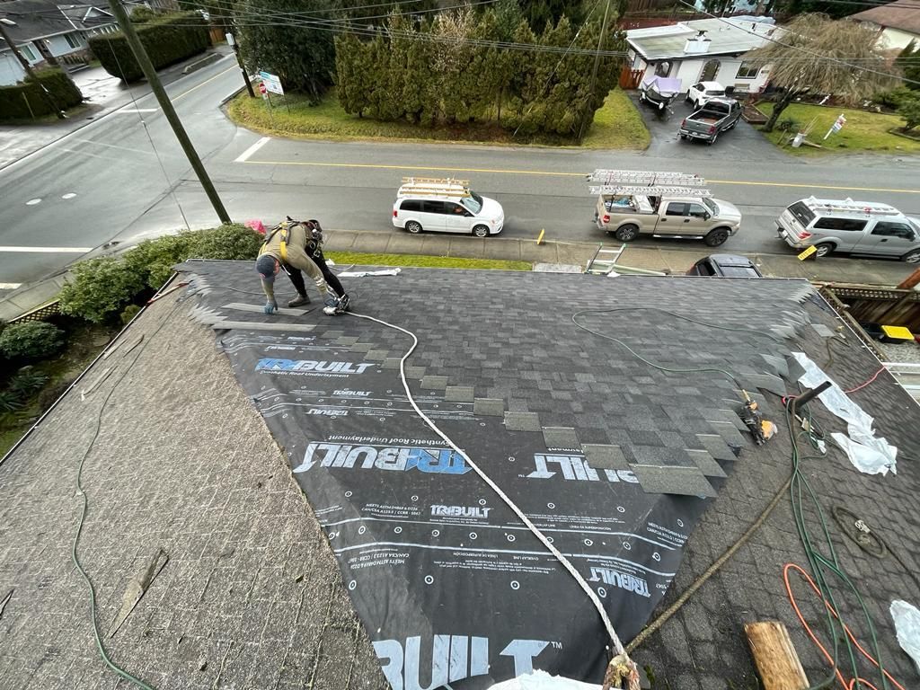 Two workers install asphalt shingles onto a residential roof over black protective underlayment.