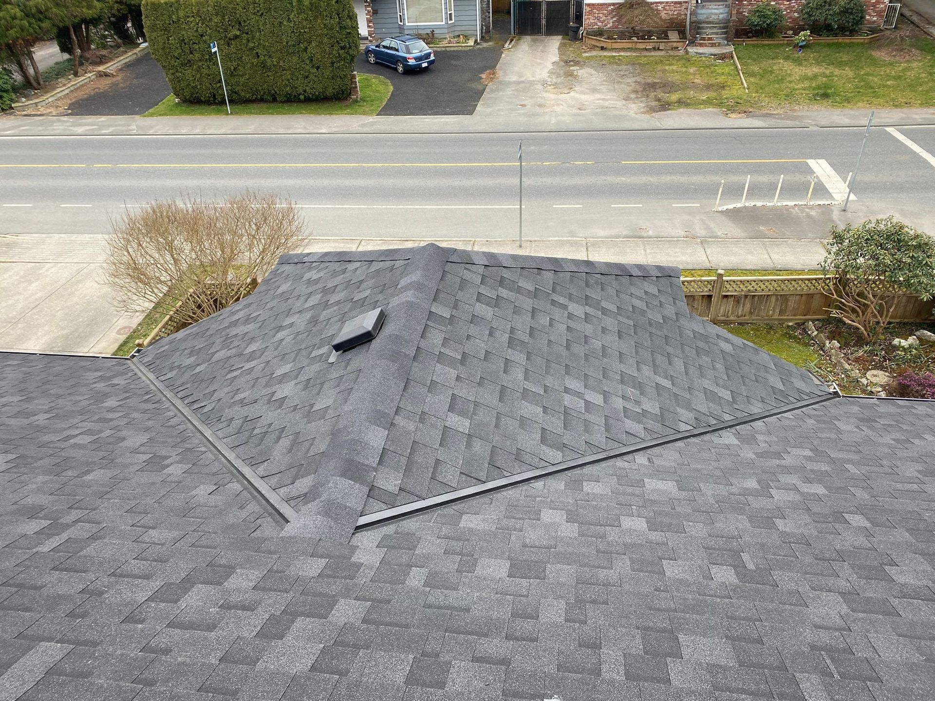 View of a house roof with asphalt shingles, overlooking a street and houses.