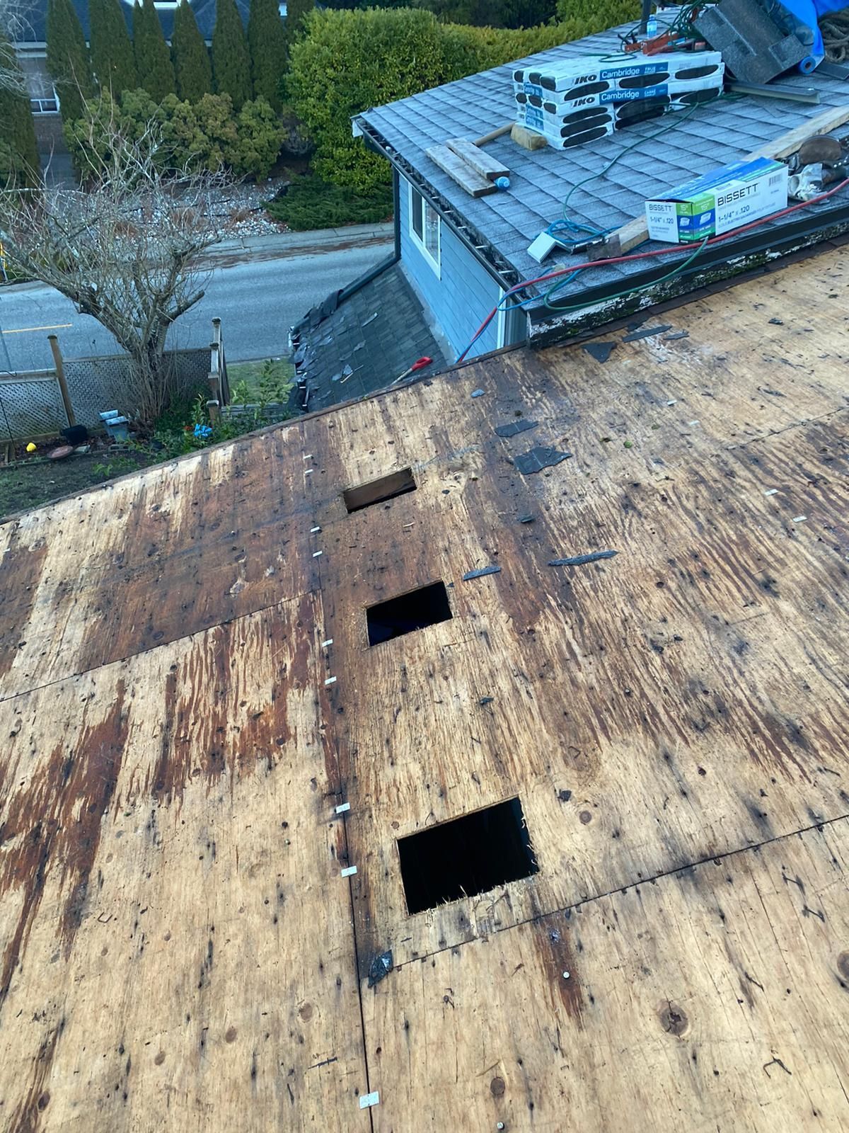 A view from above showing a wooden roof deck under renovation with three rectangular holes cut into the plywood sheeting.