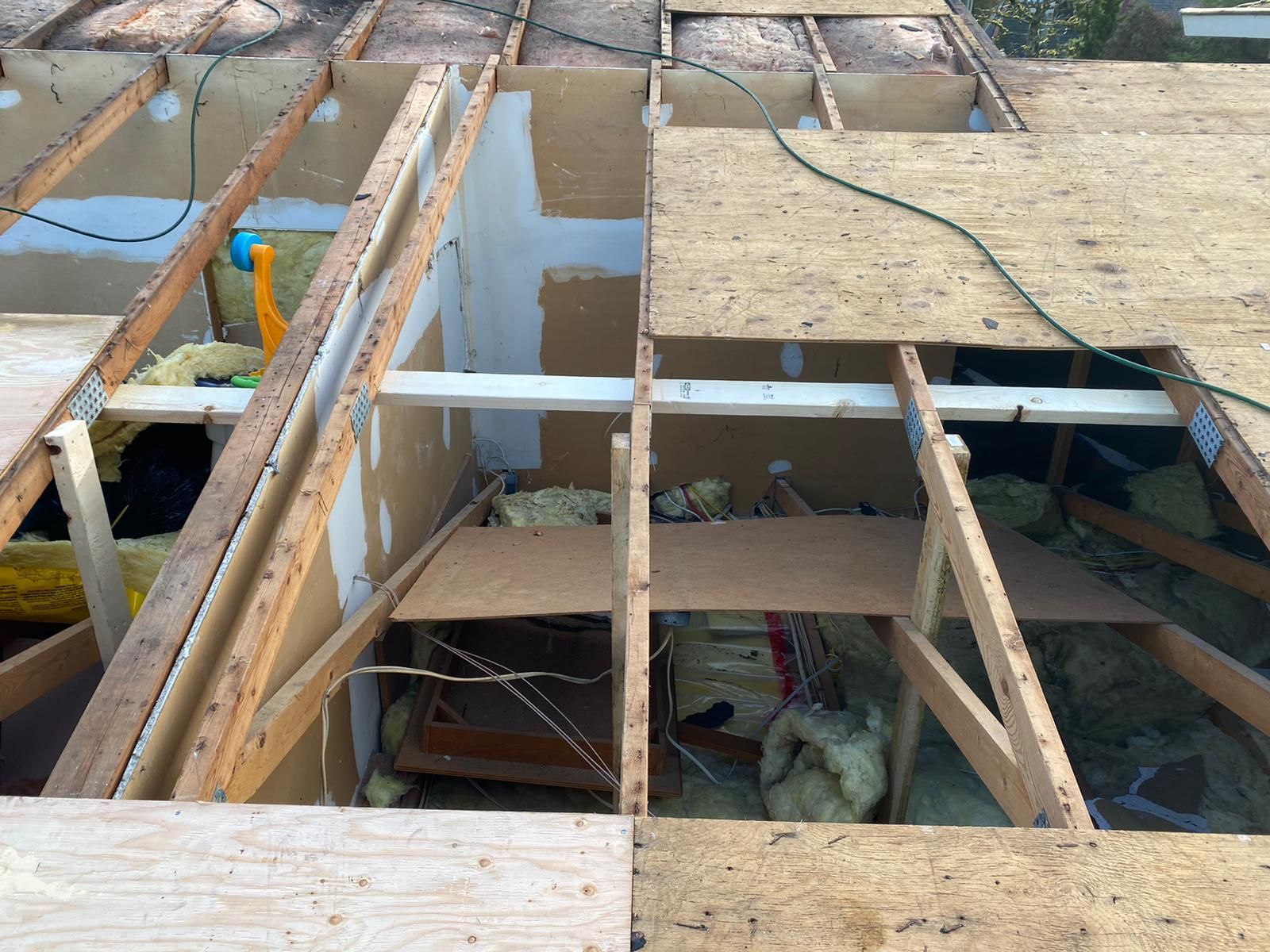 View of an open roof structure during construction, showing exposed wooden rafters, insulation, and partial plywood sheets.