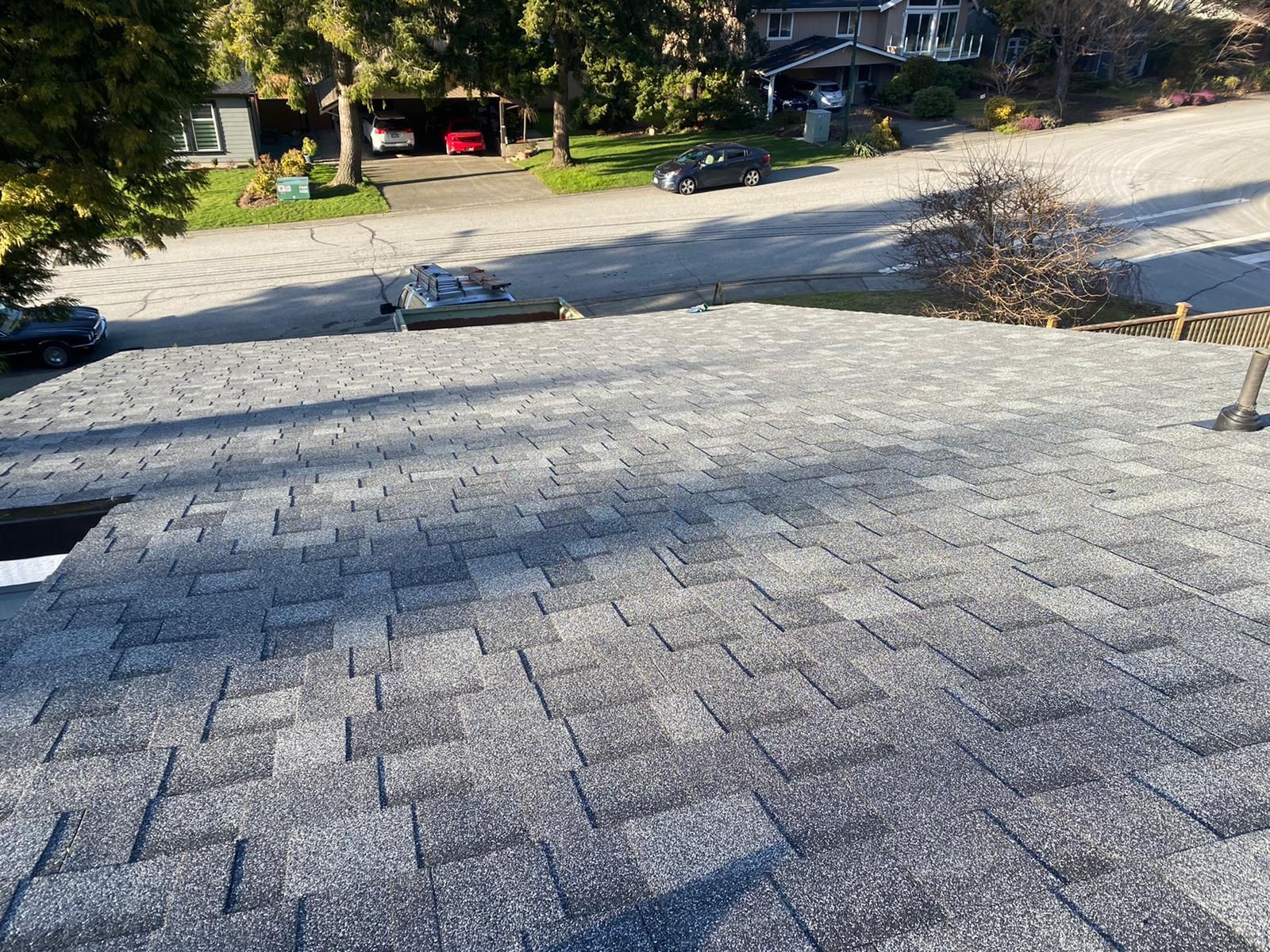 Gray asphalt shingle roof, overlooking a street and houses on a sunny day.