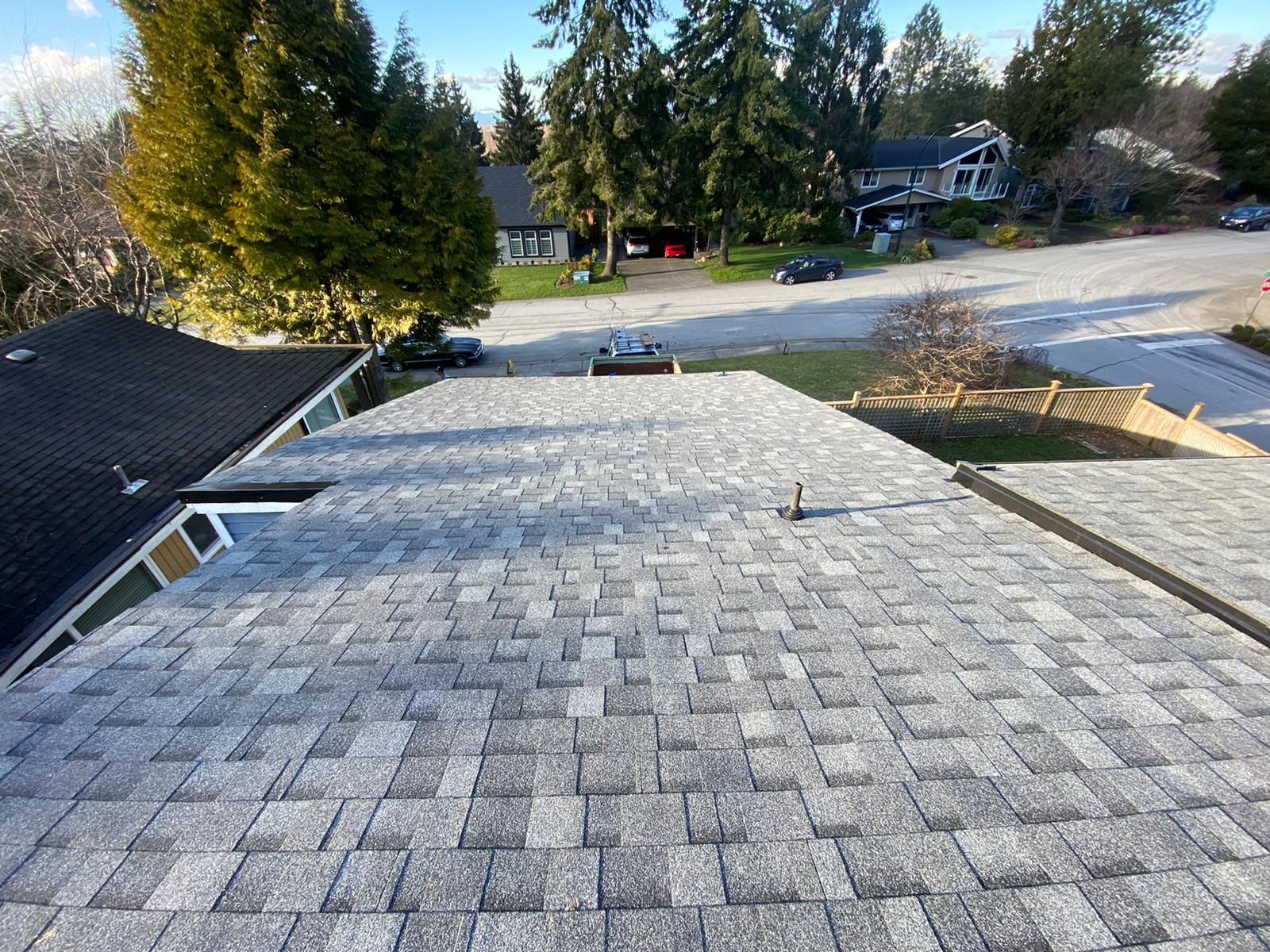 Gray shingled roof with a street and houses in the background on a sunny day.