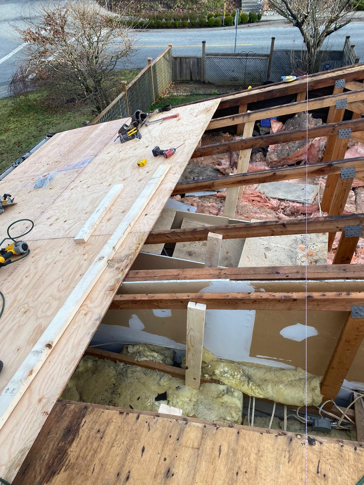 Rooftop construction: Plywood partially covers roof frame with tools and insulation visible.