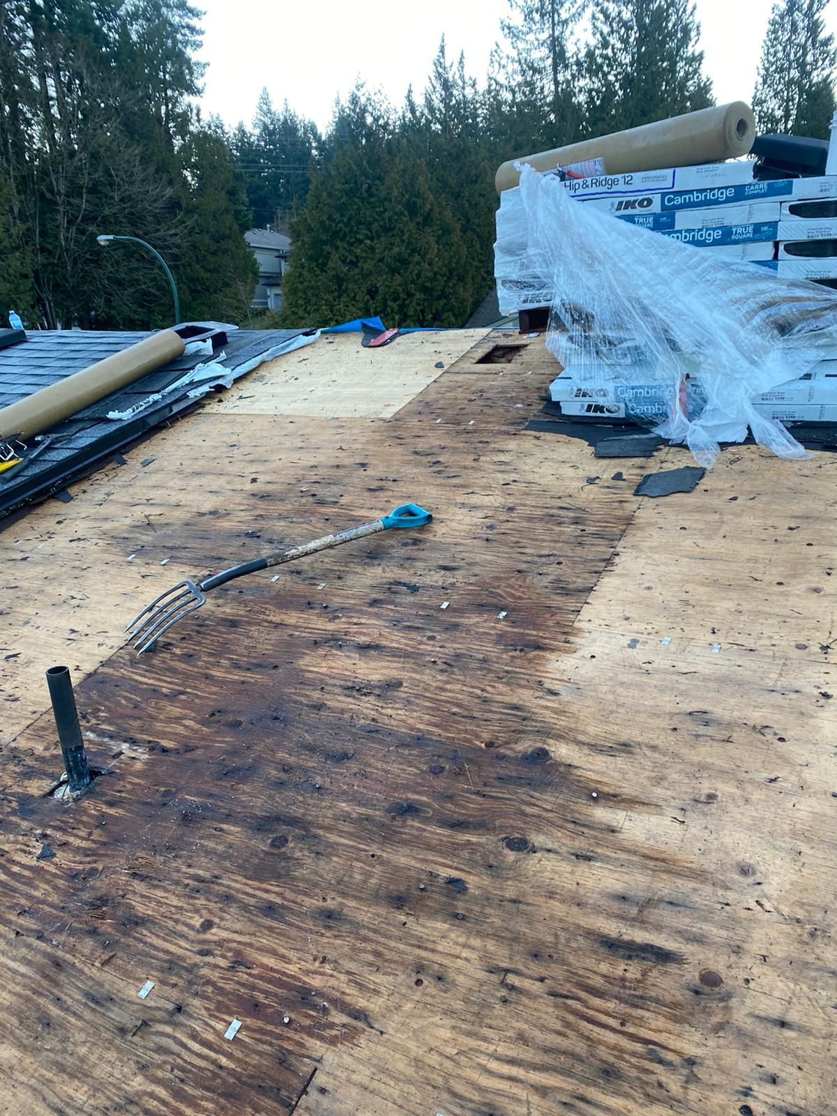 Partially covered rooftop under construction with stacked materials and trees in the background