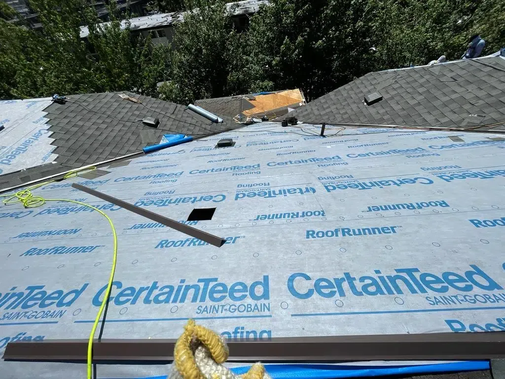 A roof under construction covered with light blue CertainTeed underlayment, showing a valley and surrounding shingles.