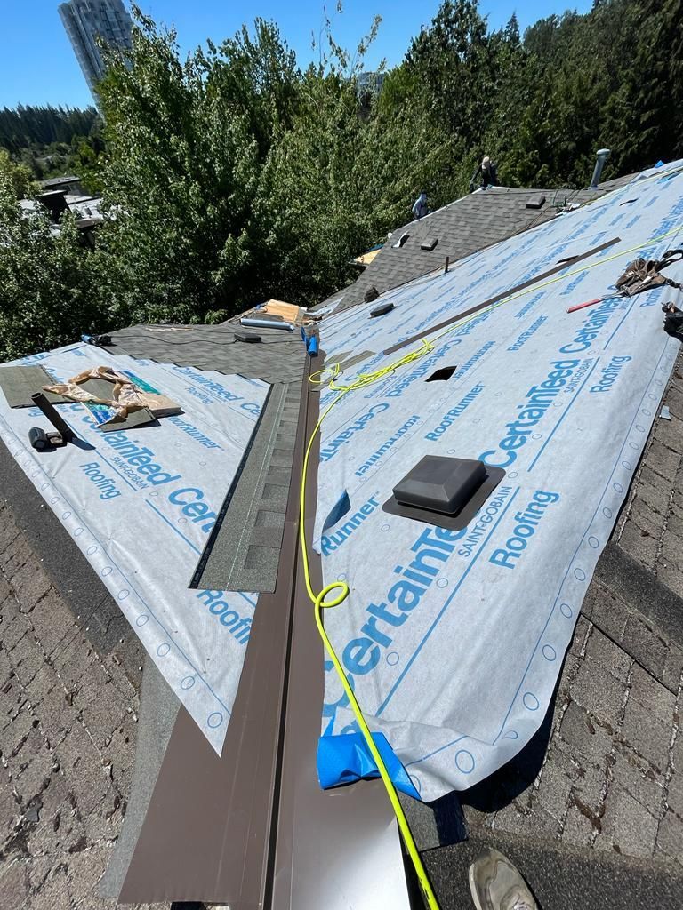 A high-angle view of a residential roof under repair, featuring blue CertainTeed underlayment, flashing, and a yellow cord.