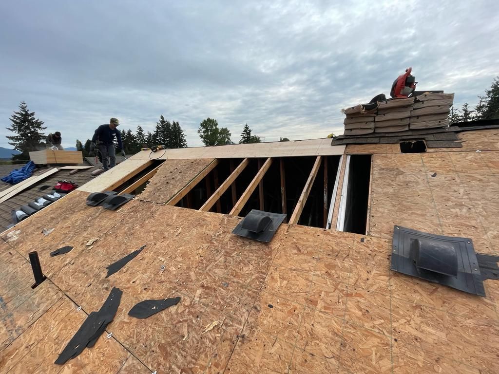 Roof under construction with workers installing plywood sheathing and roof vents on a sloped roof