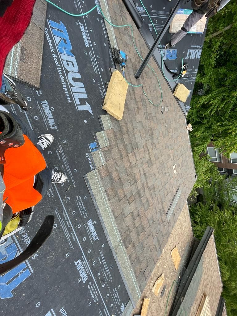 A person is standing on top of a roof covered in shingles.