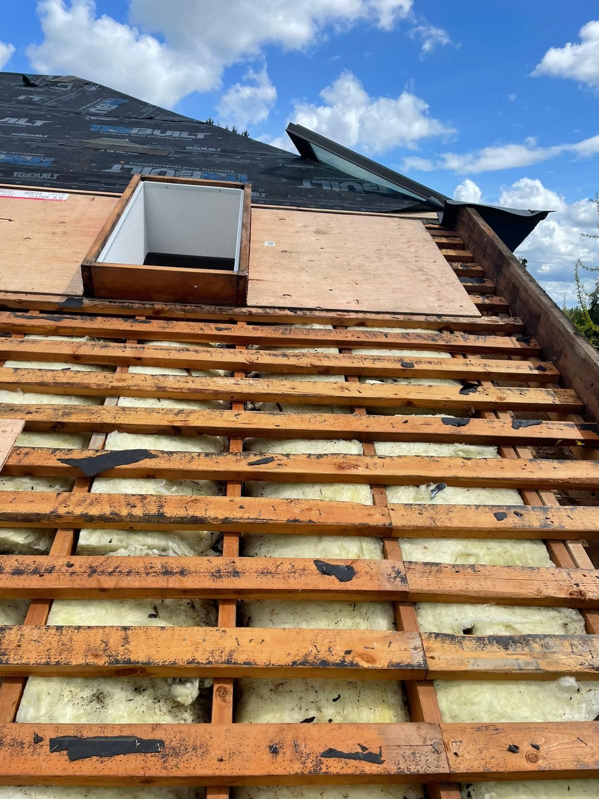 Broken roof with exposed wooden slats and an open dormer against a blue sky