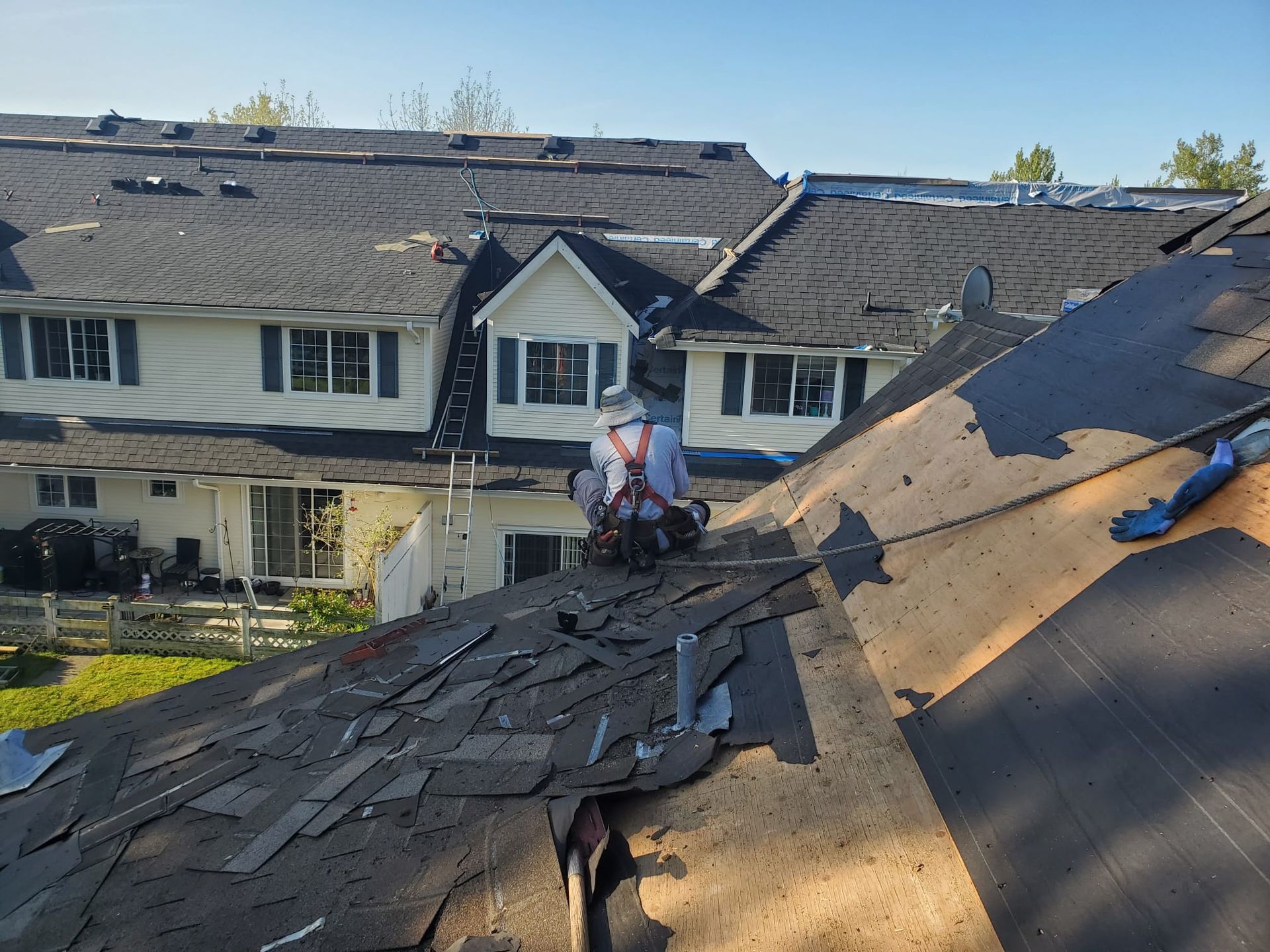 Roofer removing shingles from a house roof on a sunny day.